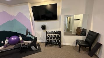 A room with a treadmill, dumbbells, a purple exercise ball, a TV, and a mirror.
