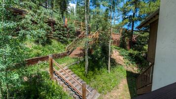 A wooden staircase surrounded by lush greenery and trees, leading to a building with a white exterior.
