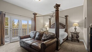A bedroom with a four-poster bed, a leather sofa, two bedside tables with lamps, and a sliding glass door leading to a balcony.