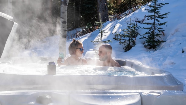 A hot tub in a snowy outdoor setting with steam rising, surrounded by snow-covered ground and trees.
