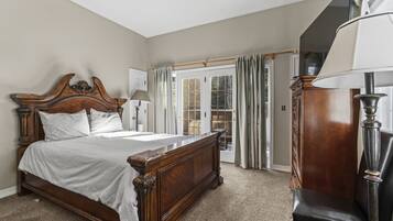 A bedroom with a large wooden bed, a chair, a lamp, and a view of the outdoors through a door.