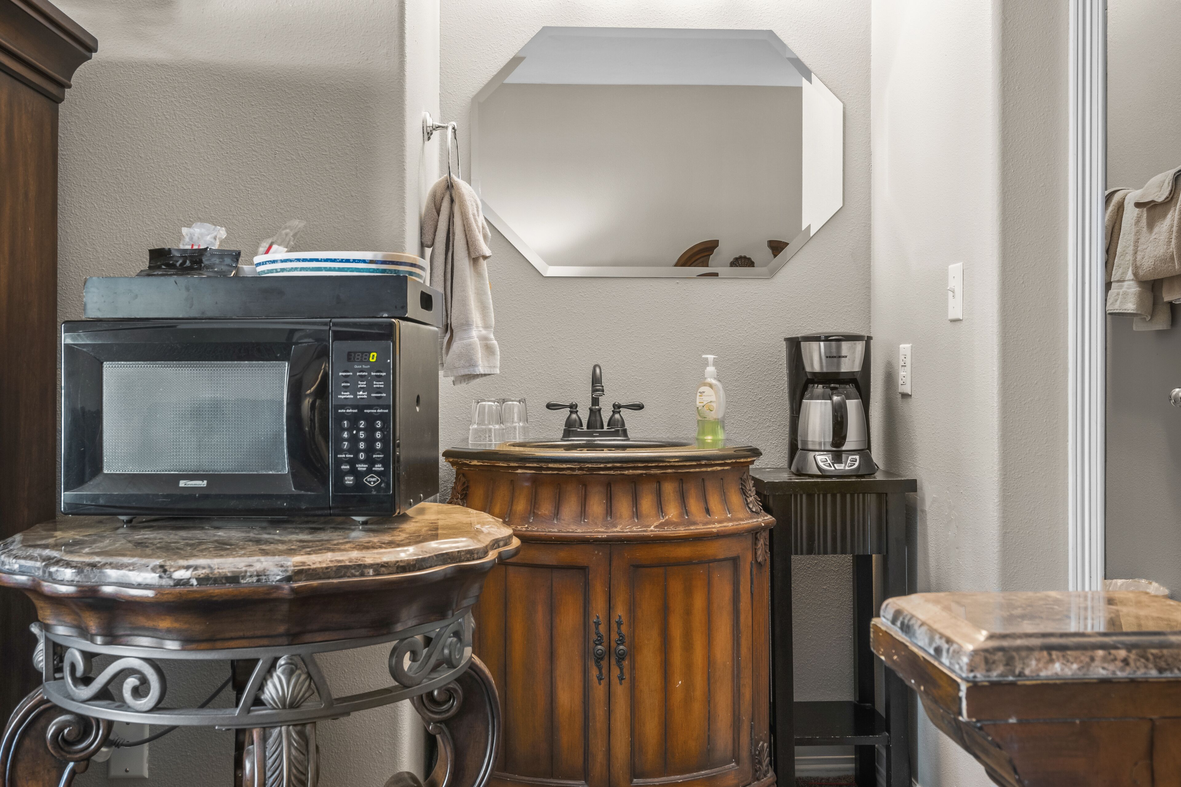 A bathroom with a sink, mirror, and a microwave on a small table.