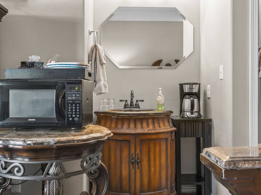 Une salle de bain avec un lavabo, un miroir et un four à micro-ondes posé sur une petite table.