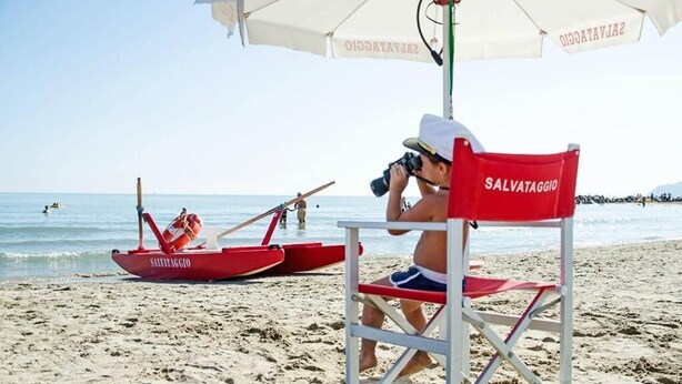 A beach scene with a lifeguard chair labeled "SALVATAGGIO" and a red lifeboat. - Hotel Atlantic Riviera (Misano Adriatico)