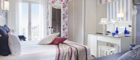 A hotel room with a bed, a desk, a mirror, and a view of the outside.