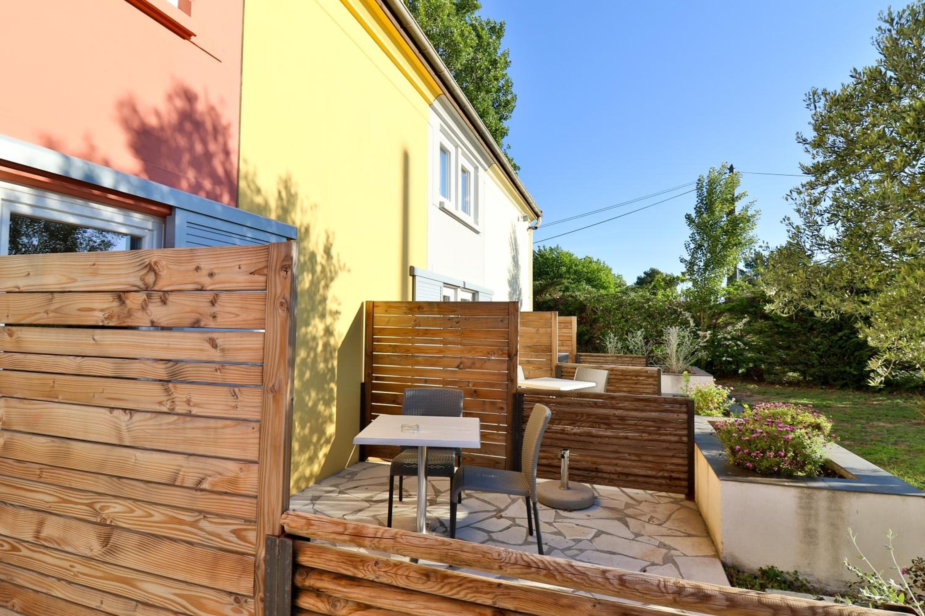 A patio area with a table and chairs, a wooden fence, and a small garden with plants.