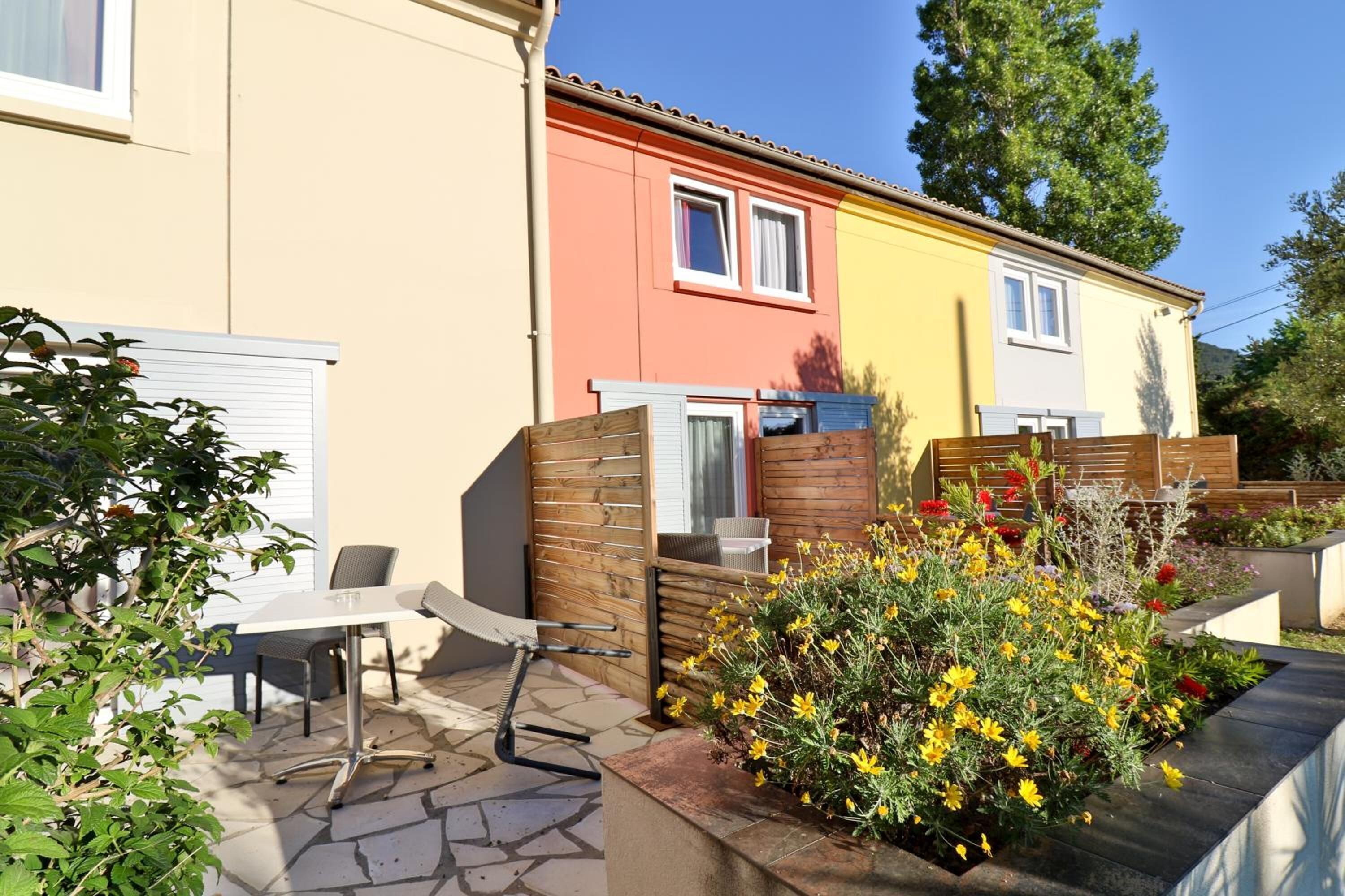 A residential area with colorful houses, a patio with a table and chairs, and a garden with yellow flowers.