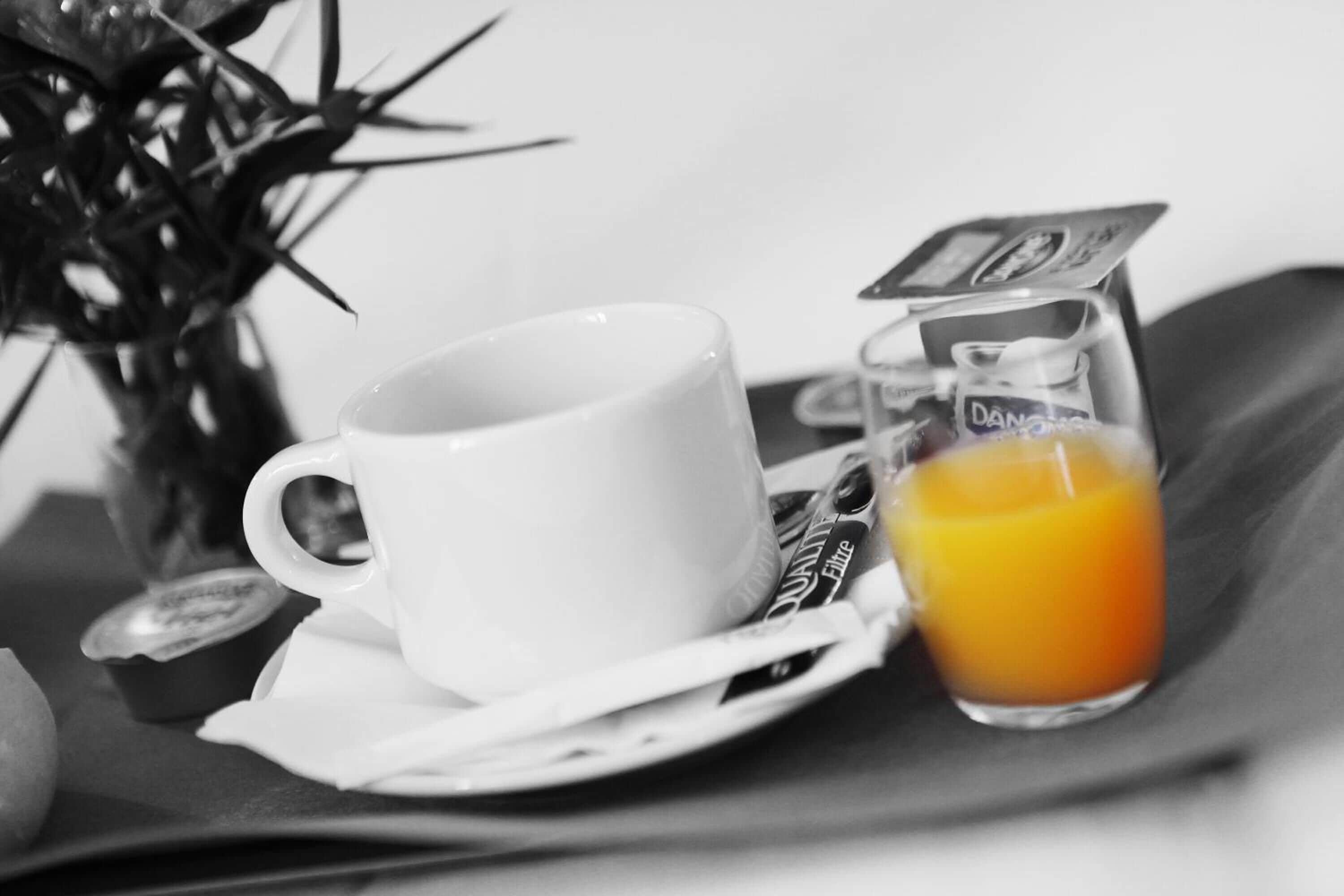 Una taza y platillo blancos con un vaso de jugo de naranja sobre una bandeja.