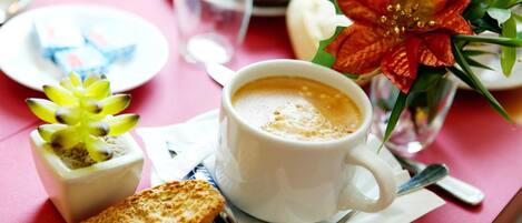 A cup of coffee with a spoon on a saucer, a small plant, and a piece of bread on a table.