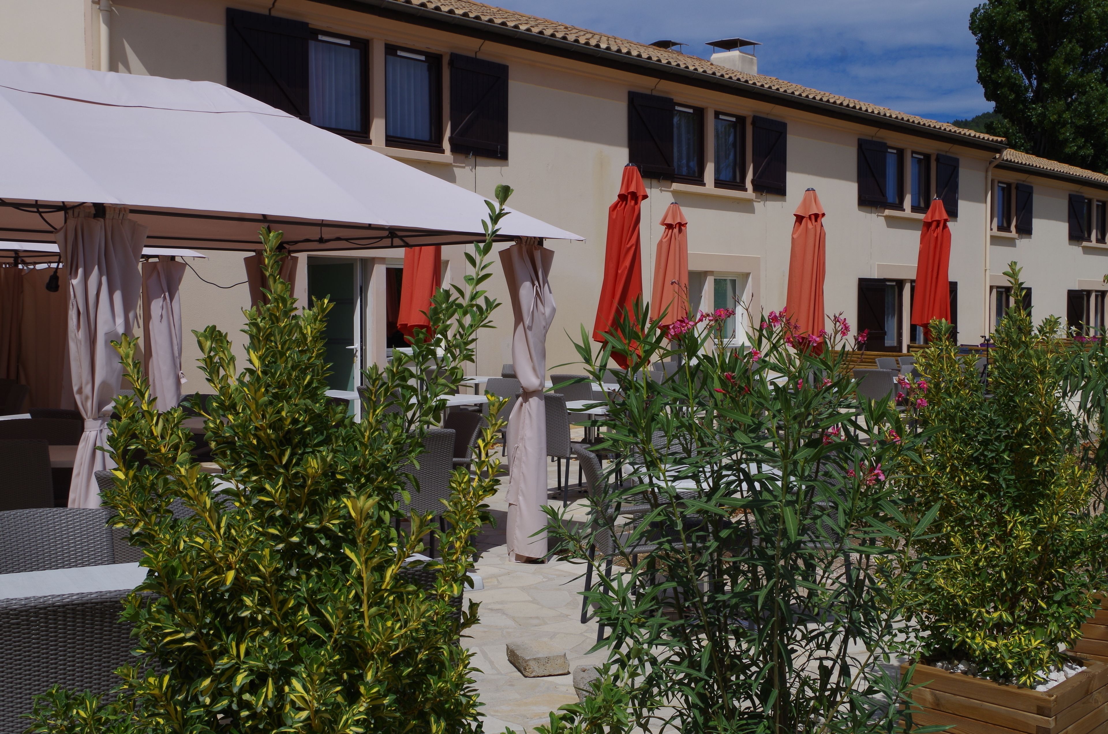Un espace extérieur aménagé en terrasse, avec des meubles en osier, des parasols rouges et des plantes en pot.