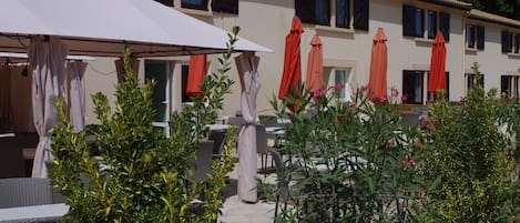 An outdoor patio area with wicker furniture, red umbrellas, and potted plants.
