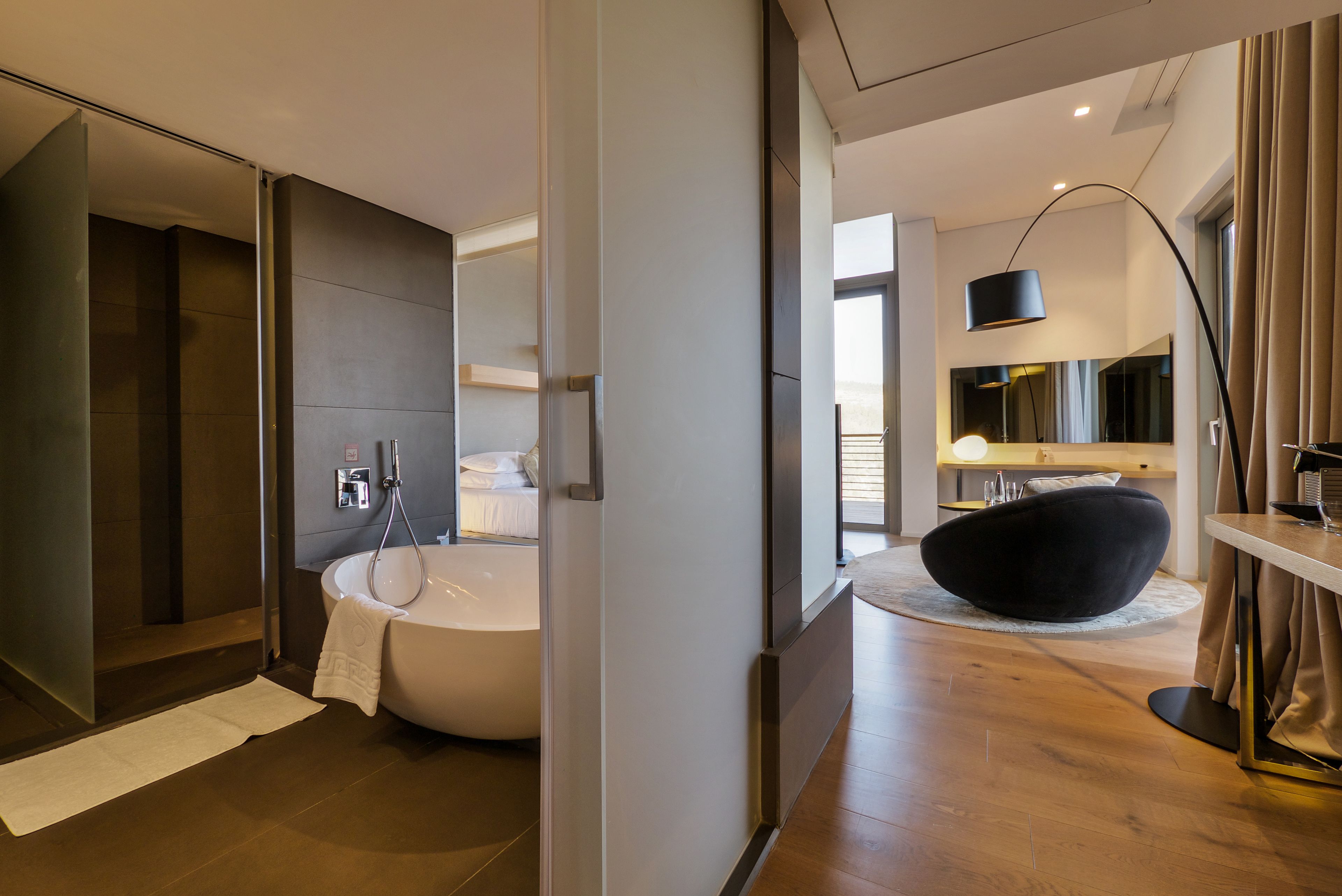 Een moderne badkamer met een vrijstaand bad, een glazen douchecabine en een zwarte relaxfauteuil.