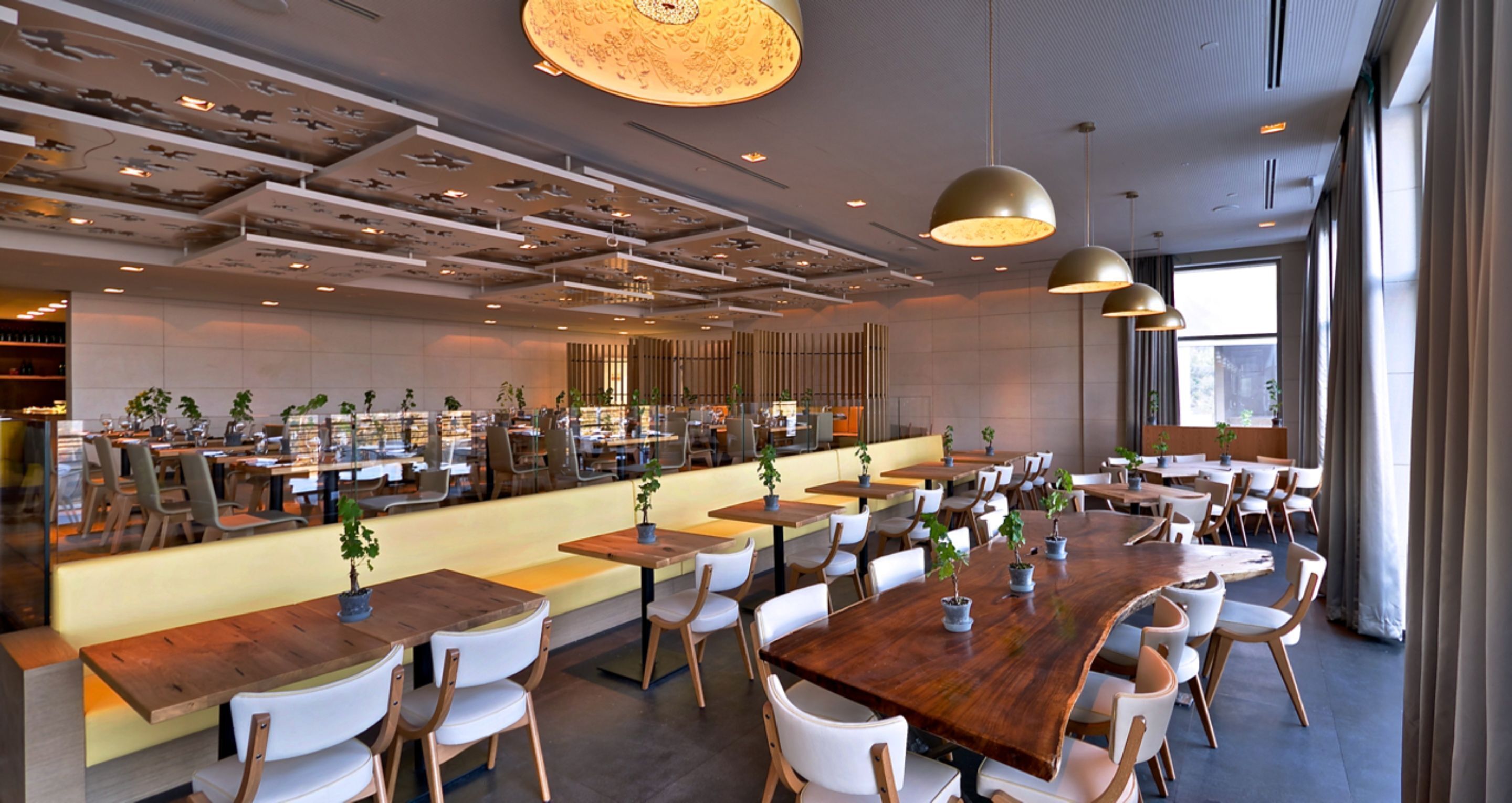 Un restaurant moderne avec des tables et des chaises en bois, des luminaires suspendus et un bar central.