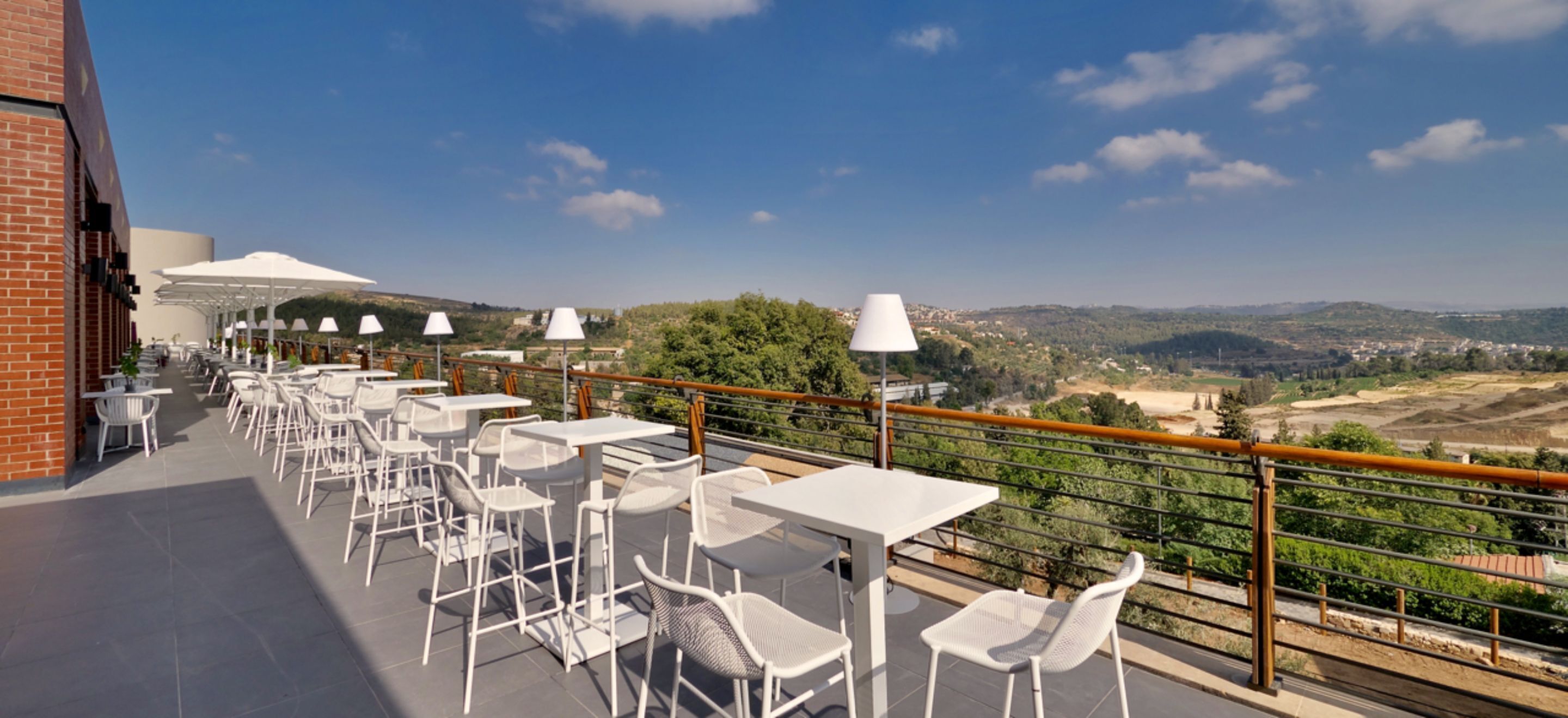 Une terrasse extérieure avec des tables et des chaises blanches, des parasols et une vue sur la campagne.