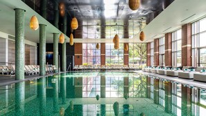 Ein großes Hallenbad mit klarem Wasser, Liegestühlen und hängenden Korblampen.