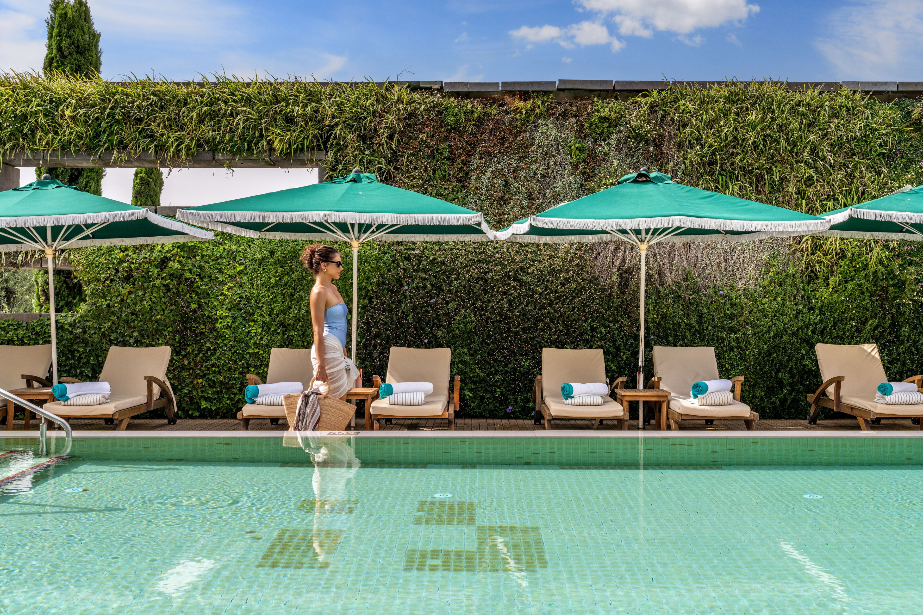 Un espace aménagé au bord de la piscine, avec des chaises longues et des parasols, une piscine carrelée et un mur végétal.