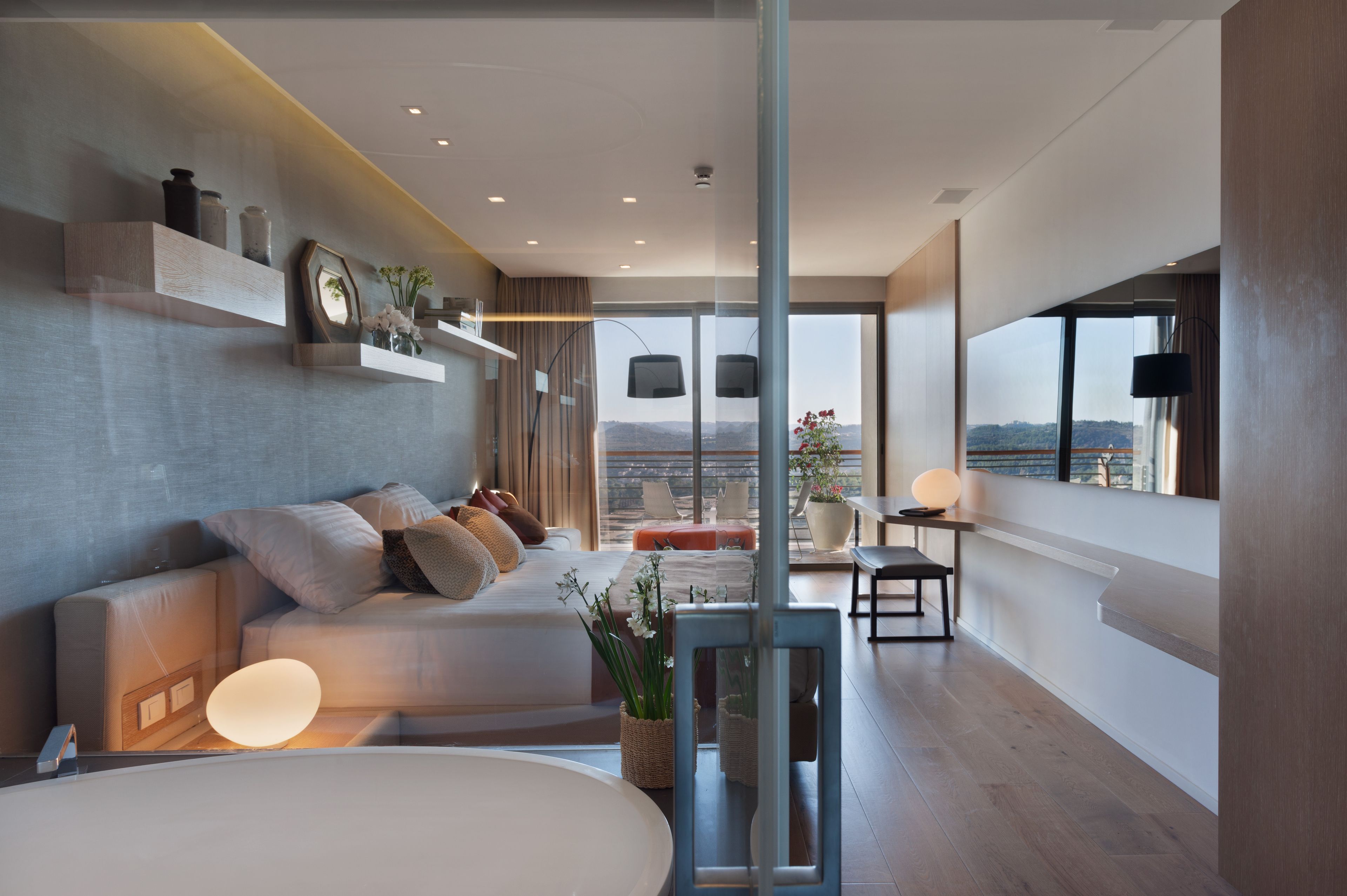 Una habitación de hotel moderna con una cama grande, una zona de estar con un sofá y sillones, una mesa de comedor y un balcón con vistas.