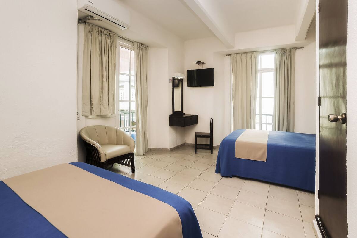 A hotel room with two beds, a chair, a desk, a television, and a window with curtains.