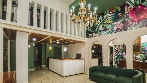 A lobby with a reception desk, a green sofa, a chandelier, and a floral mural. - Hotel Trianon (Veracruz)