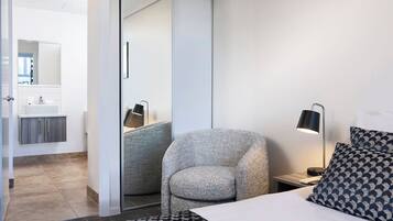 A modern hotel room with a bed, a chair, a nightstand, and a bathroom visible through a sliding door.