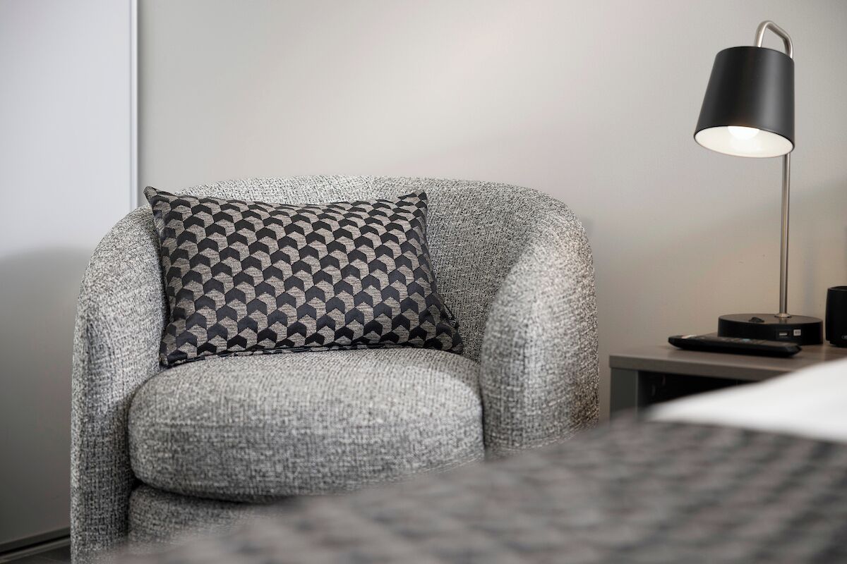 A modern armchair with a geometric patterned pillow, a sleek floor lamp, and a small side table with a remote control.