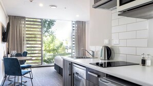A modern kitchen with a dishwasher, stove, and a dining area with blue chairs and a table. - Quest on Beaumont (Auckland)