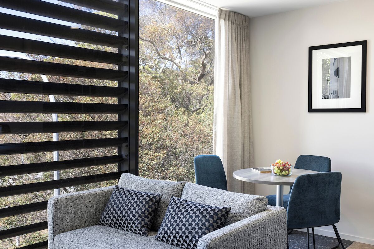 A modern room with a sofa, two chairs, a small table, and a window with a view of trees.