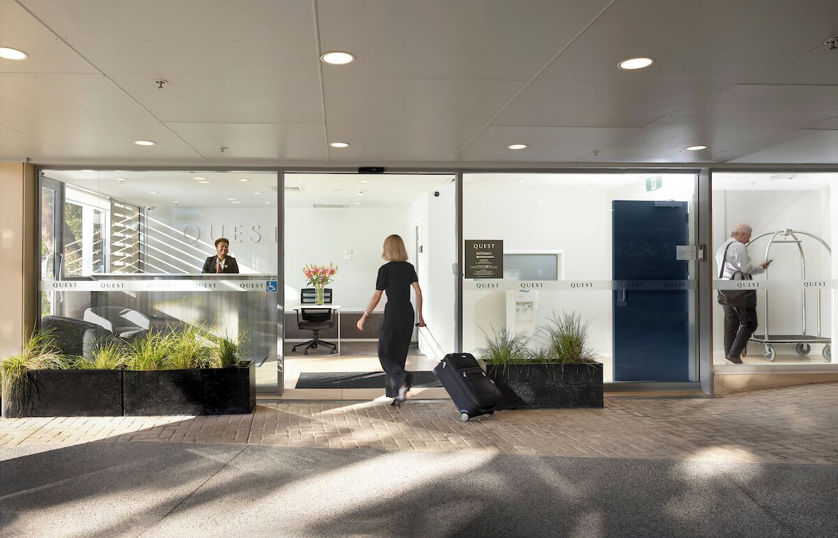 A hotel entrance with a reception desk, a waiting area with seating, and a person with luggage.