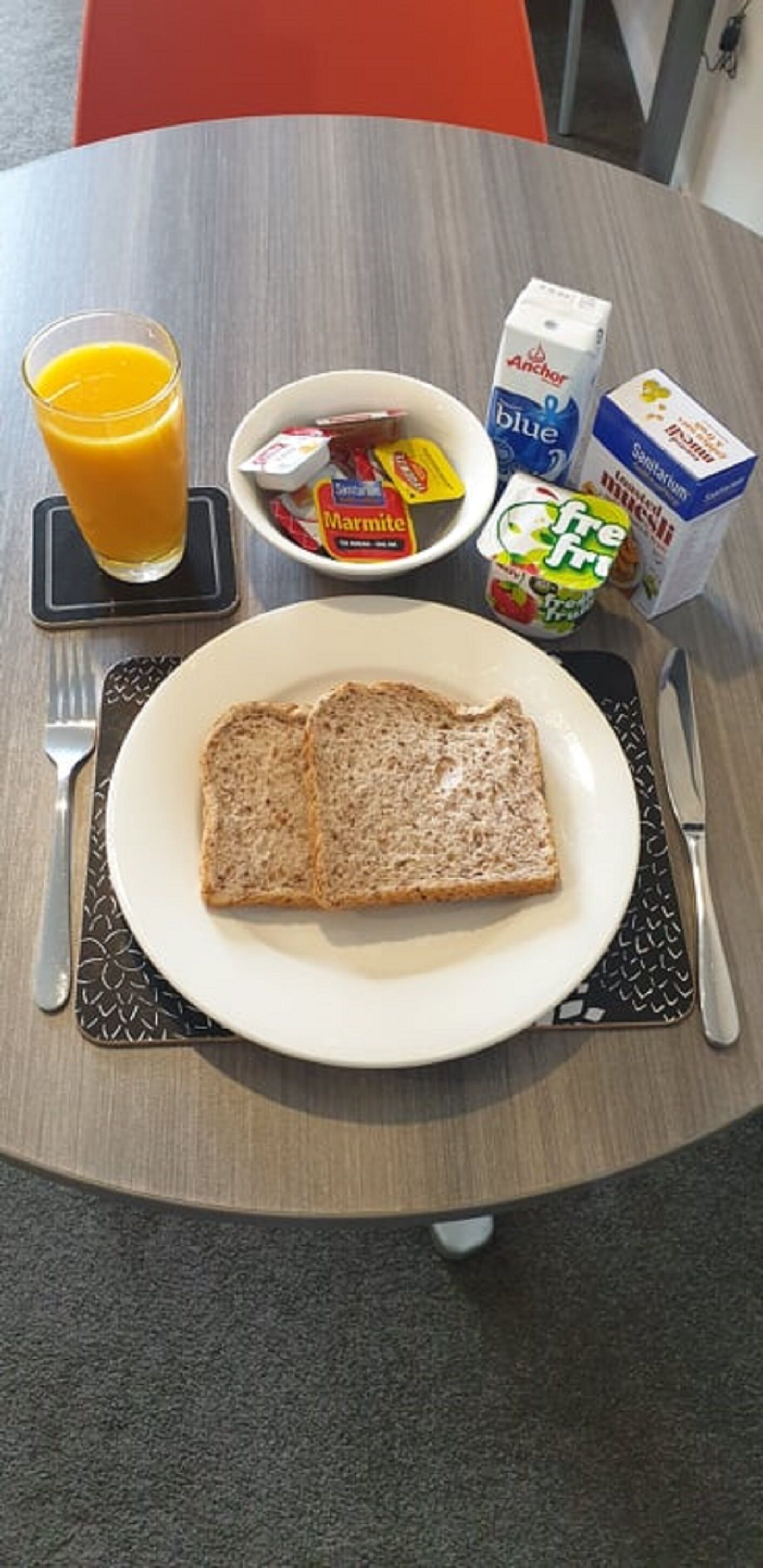 A breakfast setting with toast, marmite, orange juice, and milk cartons on a table.