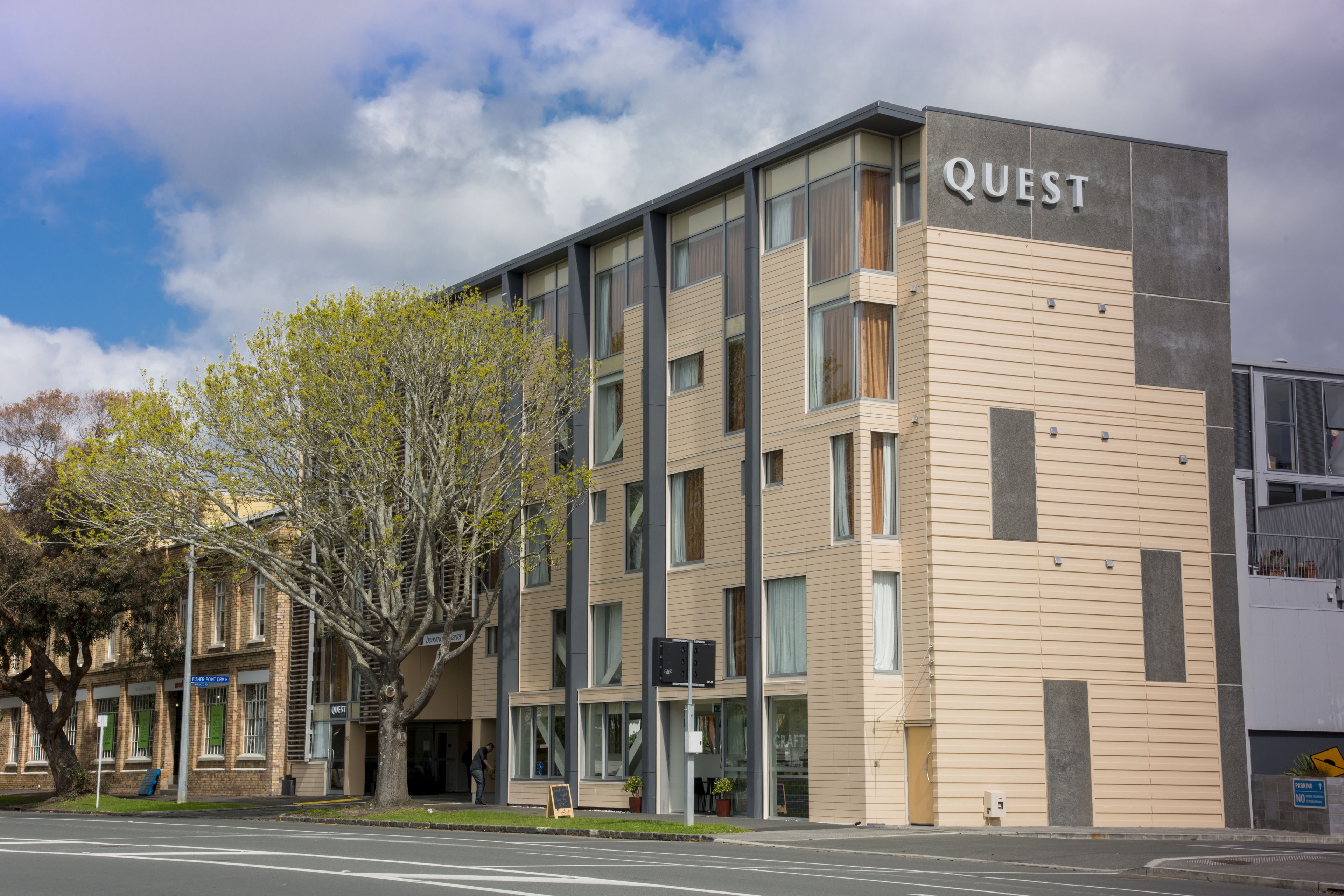 A modern building with the sign "QUEST" on the facade, featuring multiple windows and a flat roof.