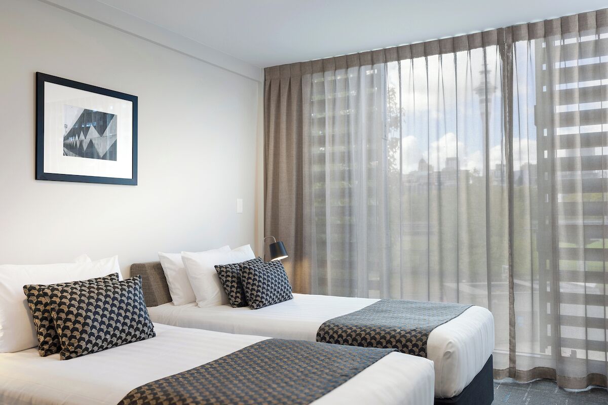 A hotel room with two beds, a framed picture on the wall, and sheer curtains.