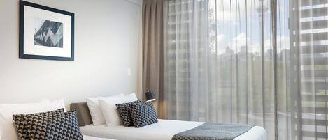 A hotel room with two beds, a framed picture on the wall, and sheer curtains.