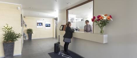A hotel reception area with a reception desk, a large mirror, and a welcome mat with the word "QUEST".