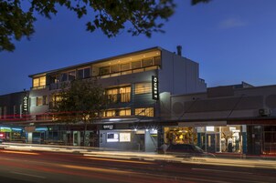 A modern hotel with a two-story structure, large windows, and a visible restaurant named 'Quest' on the ground floor.