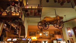 A bar with a vintage cart suspended from the ceiling, shelves with bottles, and a cash register.
