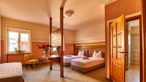 A hotel room with two beds, a sitting area with a chair and table, and a bathroom visible through an open door.