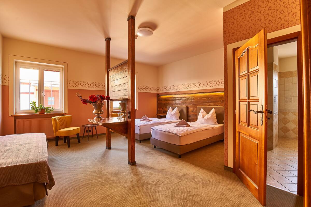 A hotel room with two beds, a sitting area with a chair and table, and a bathroom visible through an open door.