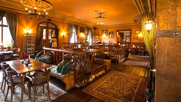 A spacious room with a large wooden dining table, multiple chairs, a vintage carriage, and a chandelier.
