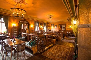 A spacious room with a large wooden dining table, multiple chairs, a vintage carriage, and a chandelier. - Hotel U Šimla (Karlovy Vary)