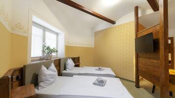 A hotel room with two beds, a TV, a window with blinds, and a plant.