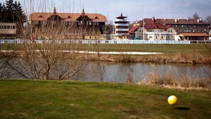 A golf ball on a grassy field with a pond and buildings in the background.