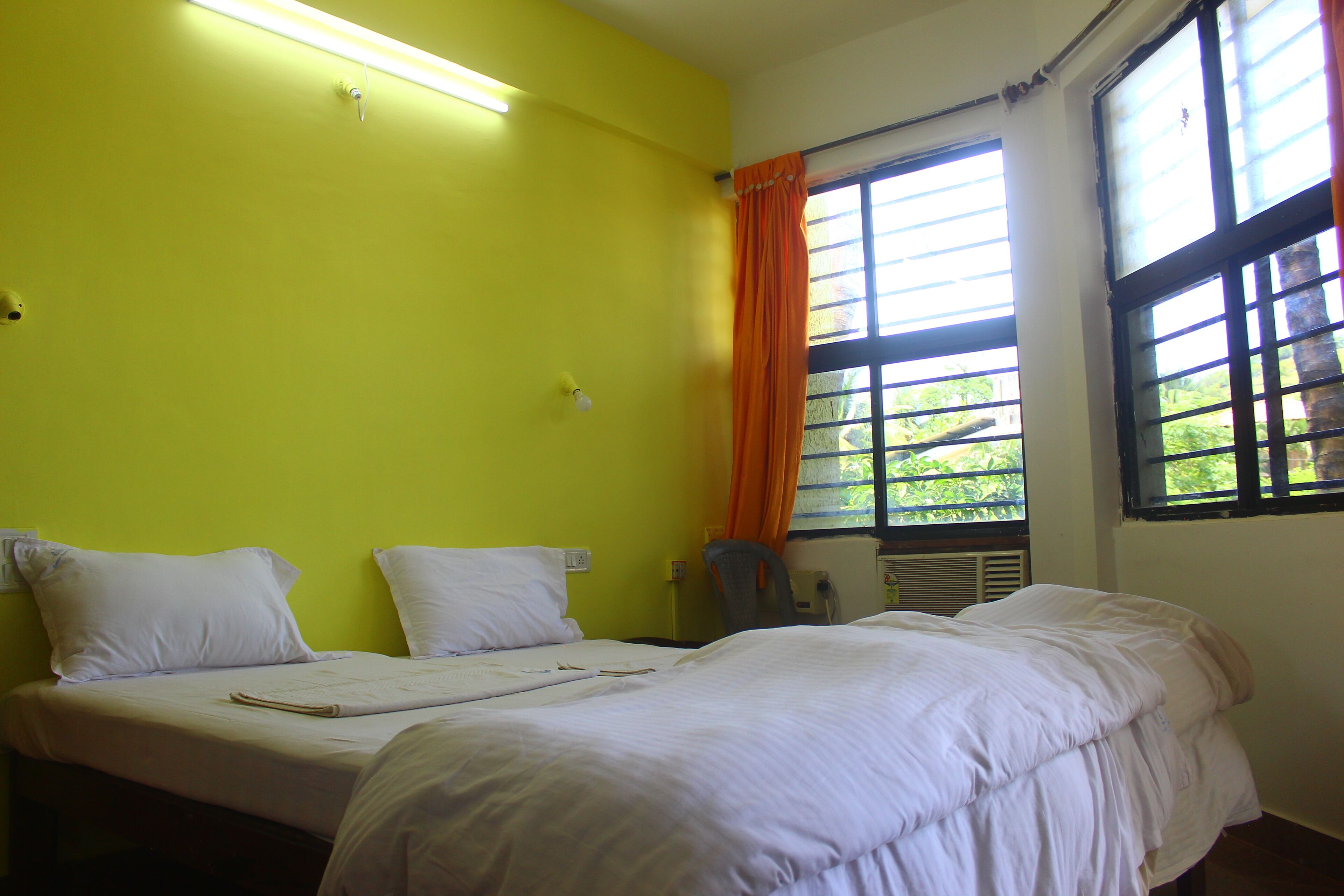 Una habitación con dos camas, una ventana con cortinas naranjas y una silla.