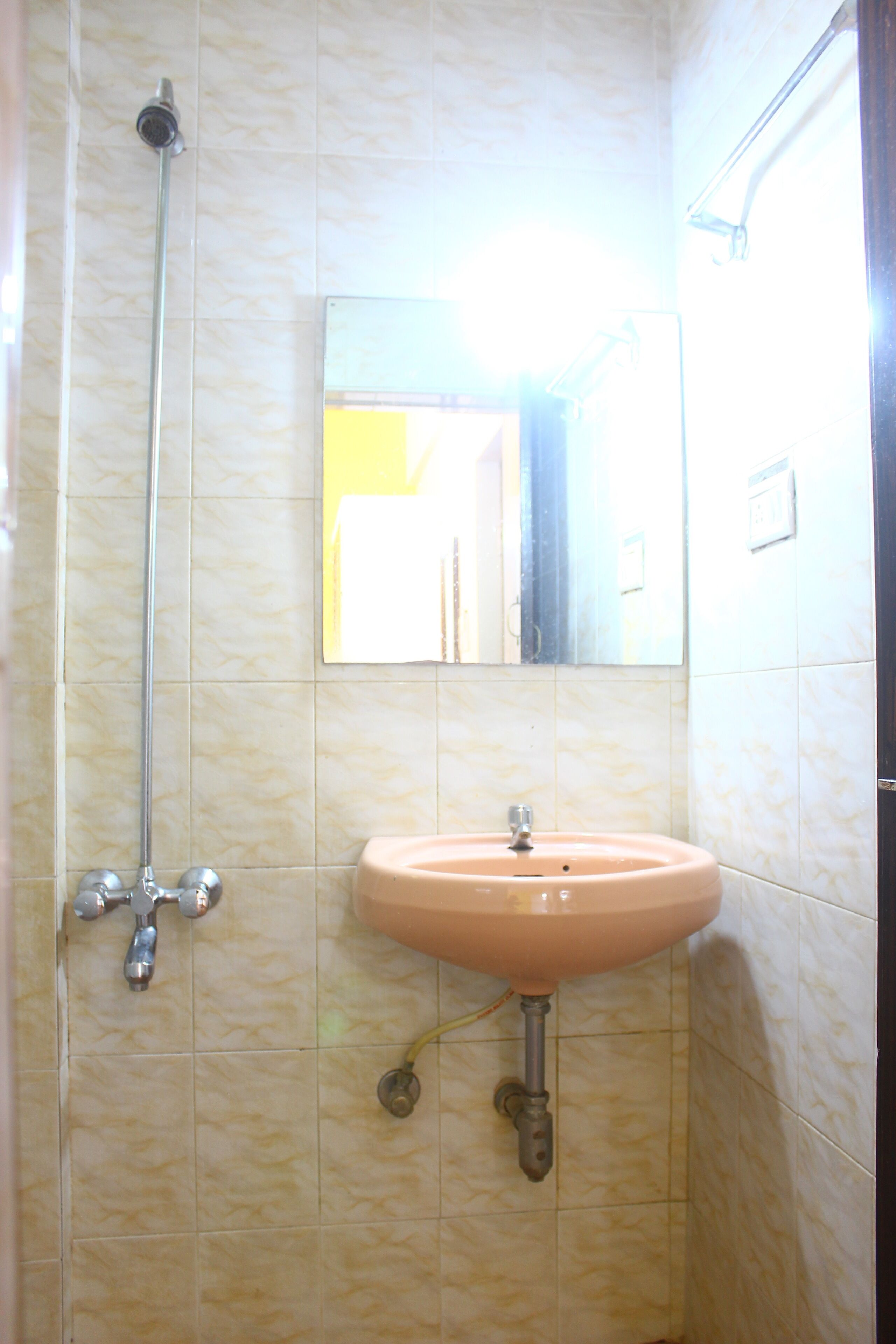 Um banheiro com parede revestida de azulejos bege, pia rosa e chuveiro com barra deslizante.