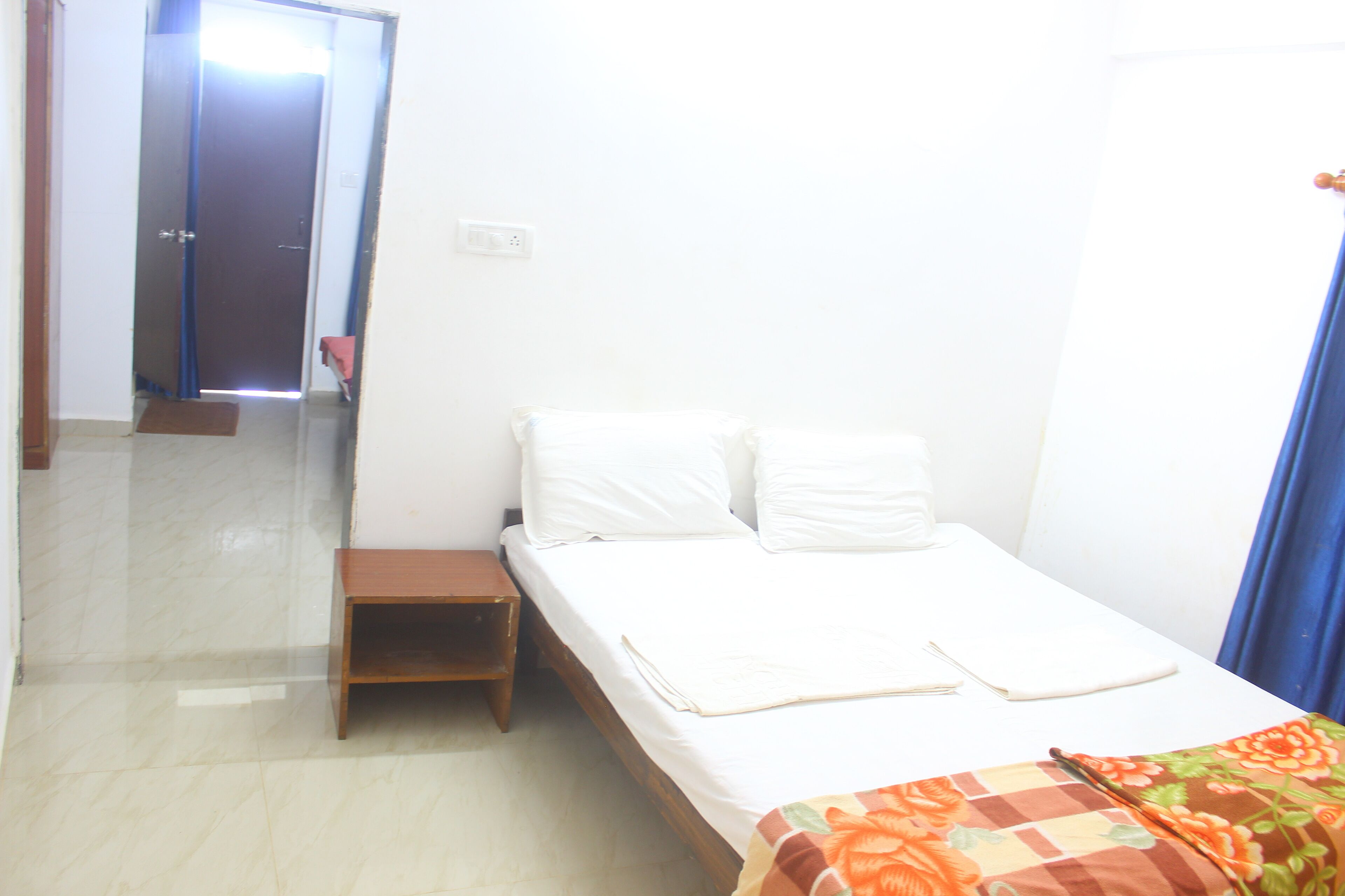A small, clean room with a bed, a nightstand, and a door leading to another room.