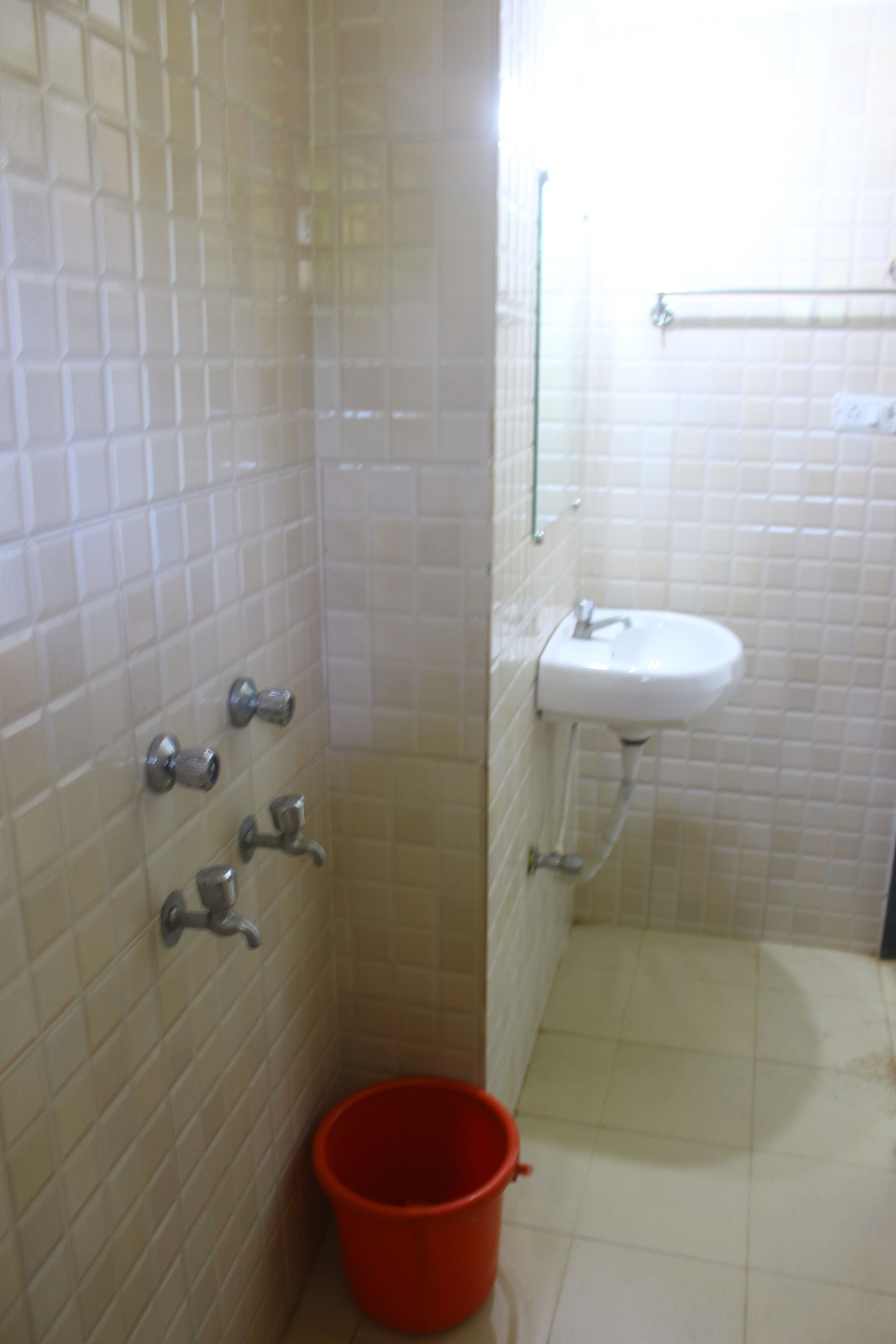 A bathroom with white tiled walls, a sink, and a red bucket.