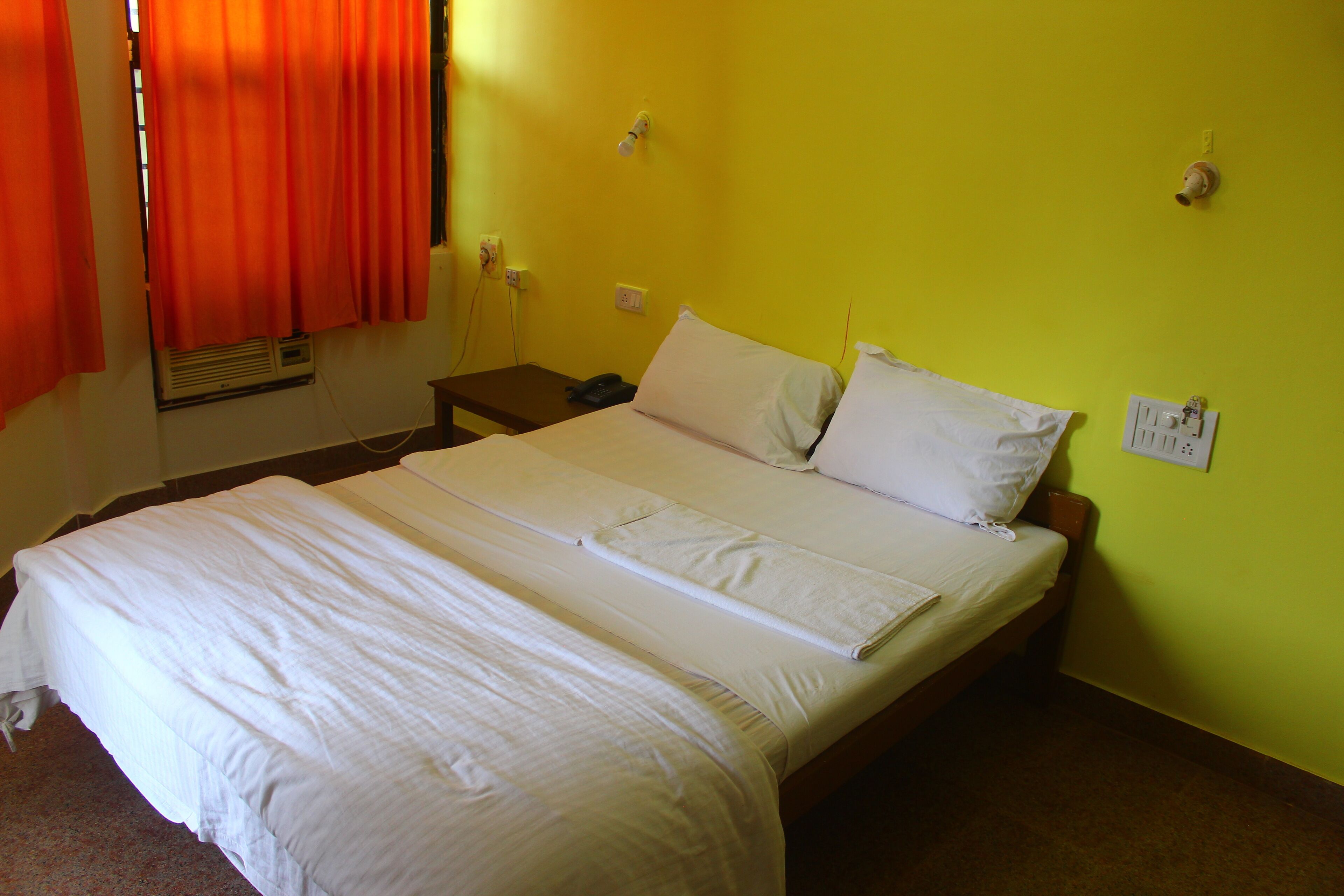 A neatly made bed with white linens in a room with yellow walls.