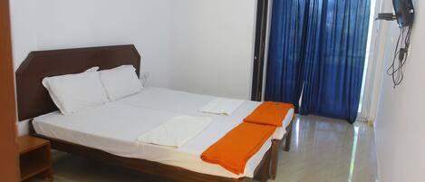 A neatly made bed with white linens and an orange blanket, a wooden nightstand, and a wall-mounted TV.