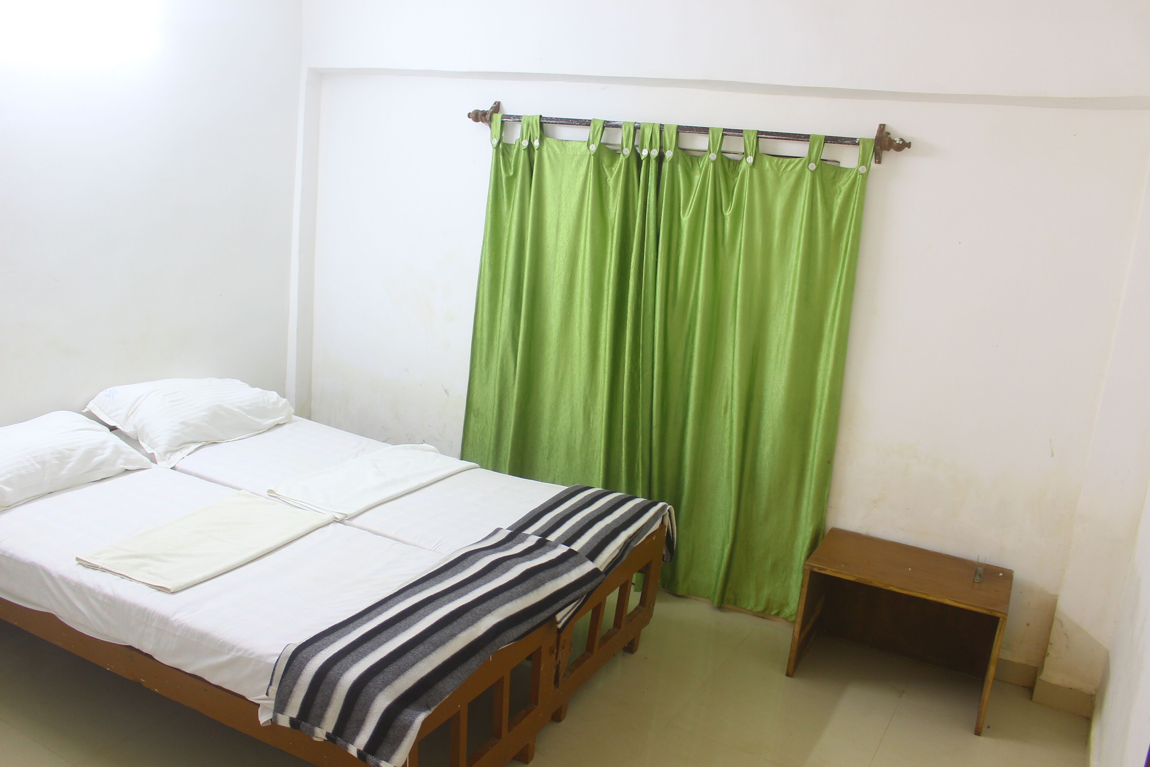 A single bed with white bedding, a green curtain, and a small wooden nightstand.