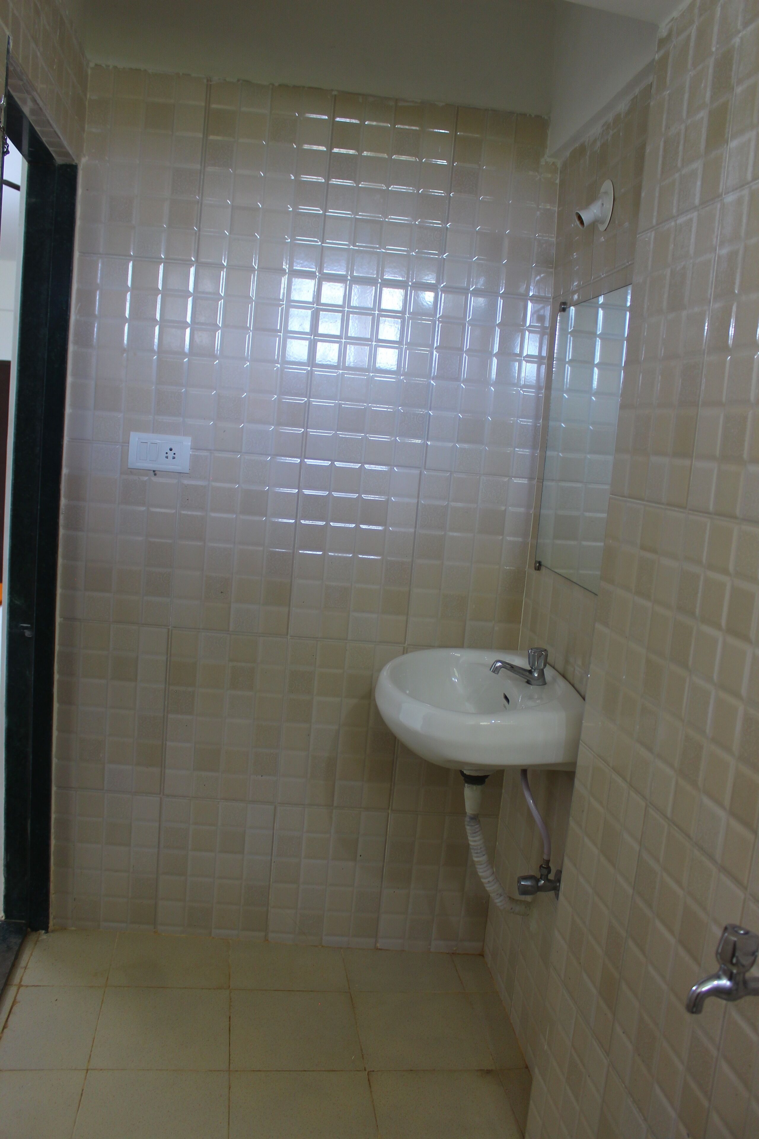 A bathroom with beige tiled walls, a white sink with a mirror, and a showerhead.