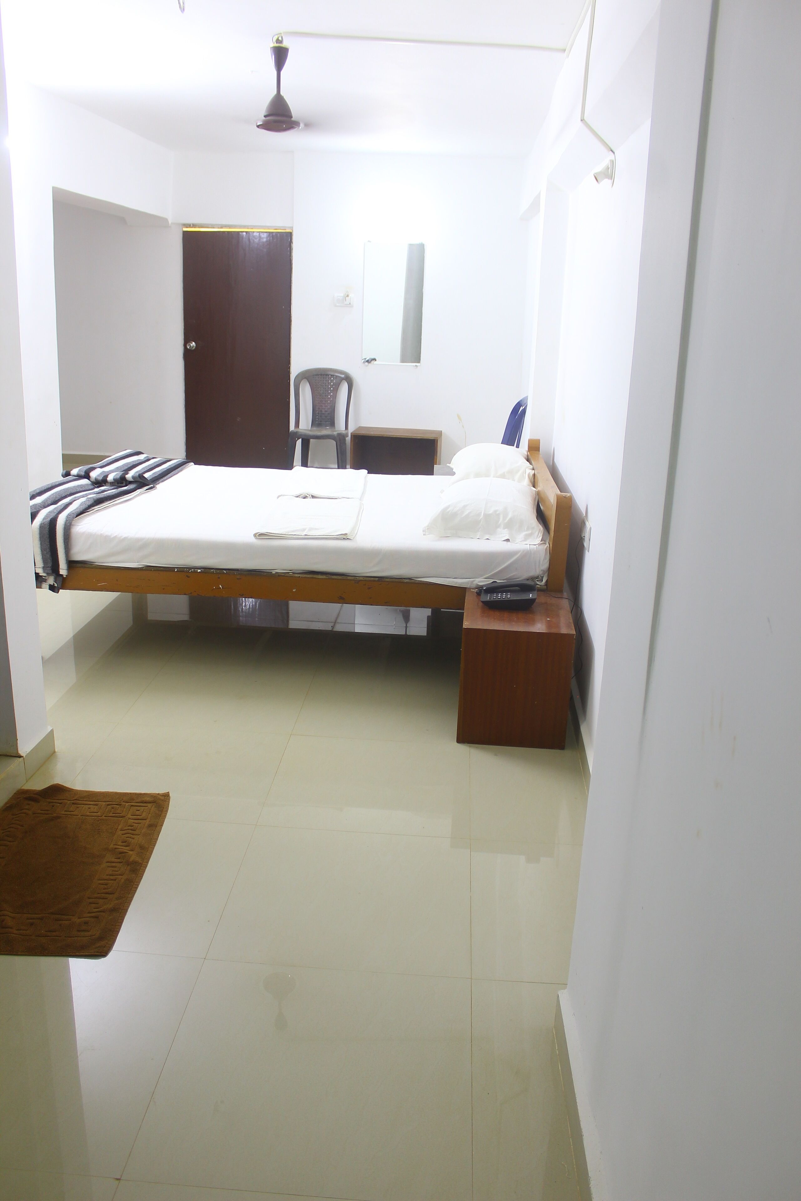 A small, clean room with a single bed, a bedside table, a chair, and a wardrobe.